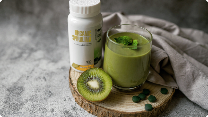 Maxler Organic Spirulina bottle alongside a green smoothie and fresh kiwi, highlighting its natural ingredients and health benefits