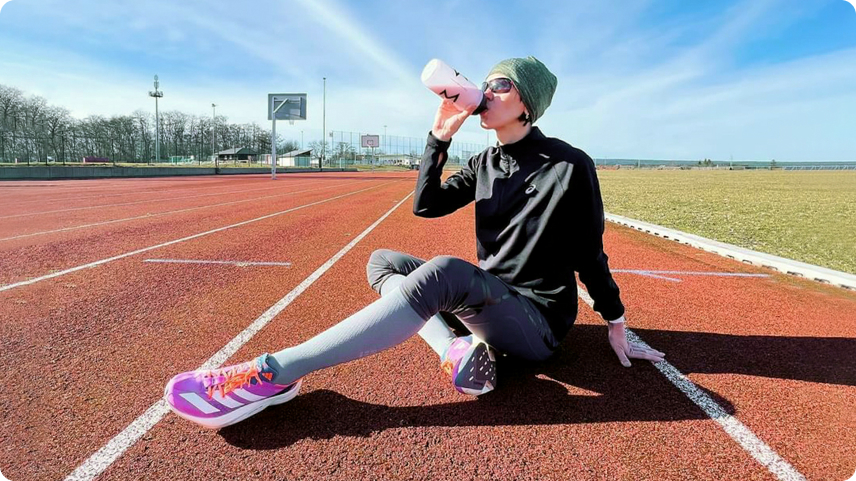 Athlete sitting on a running track, drinking from a Maxler shaker bottle as part of a sugar-conscious fitness routine