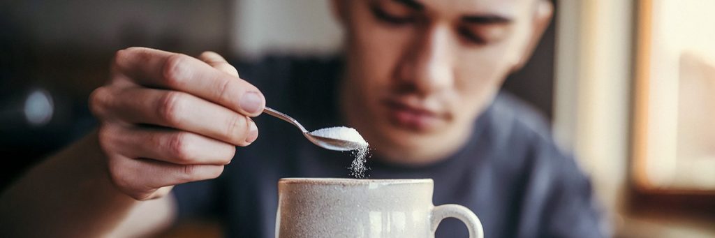 Man adding sucralose sweetener to a cup of coffee as a sugar alternative